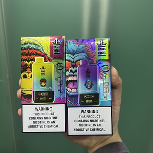 Hand holding two colorful Bang King disposable vape boxes—one yellow-green and one purple-blue with stylized gorilla artwork and brand logos, each bearing a prominent warning that the product contains nicotine and that nicotine is an addictive chemical.