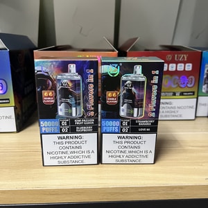 Two boxed disposable vape devices side by side on a store shelf, each labeled "50,000 puffs" and "2 flavors in 1" with flavor names (left: kiwi, passion fruit, guava; right: strawberry, banana) and a prominent nicotine warning on the front.