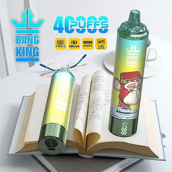 Dos dispositivos de vapeo desechables con degradado verde metálico con la marca "BANG KING", uno en posición vertical con una etiqueta de mono de dibujos animados y una pantalla LED, el otro tumbado de lado, descansando sobre un libro abierto junto a anteojos y un plato, con íconos promocionales que dicen "40000 inhalaciones" y carga tipo C.